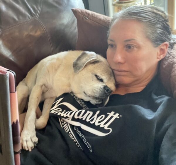 Julie Lorraine sitting on the couch with her dog curled against her.